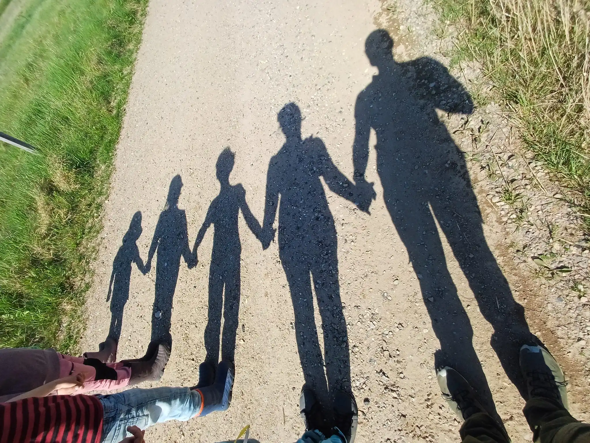 Familie hält Händchen auf Schotterweg – Schatten von Eltern und Kindern im Sonnenlicht