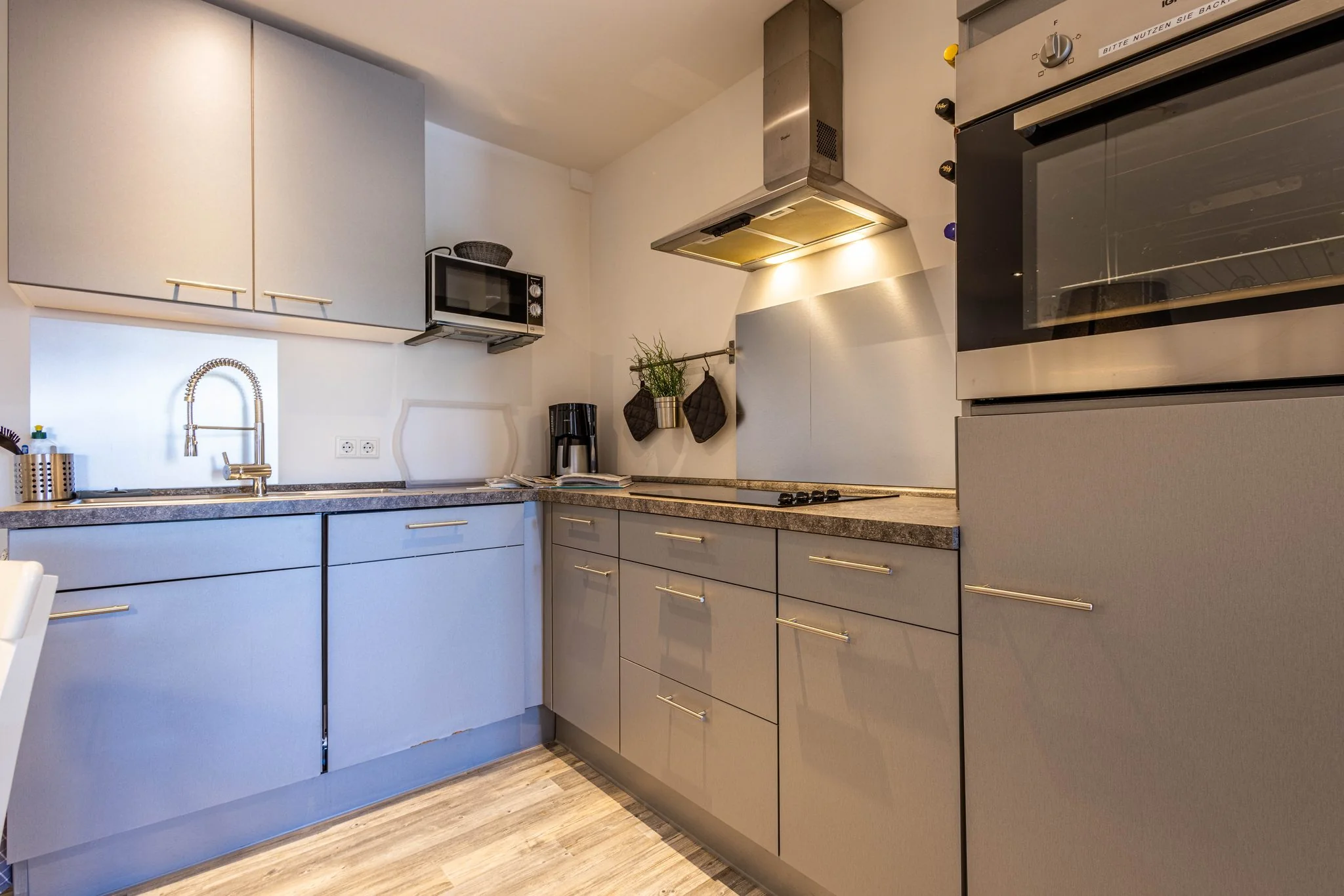Moderne Einbauküche mit grauen Hochglanzfronten, Induktionskochfeld, Backofen und Dunstabzugshaube