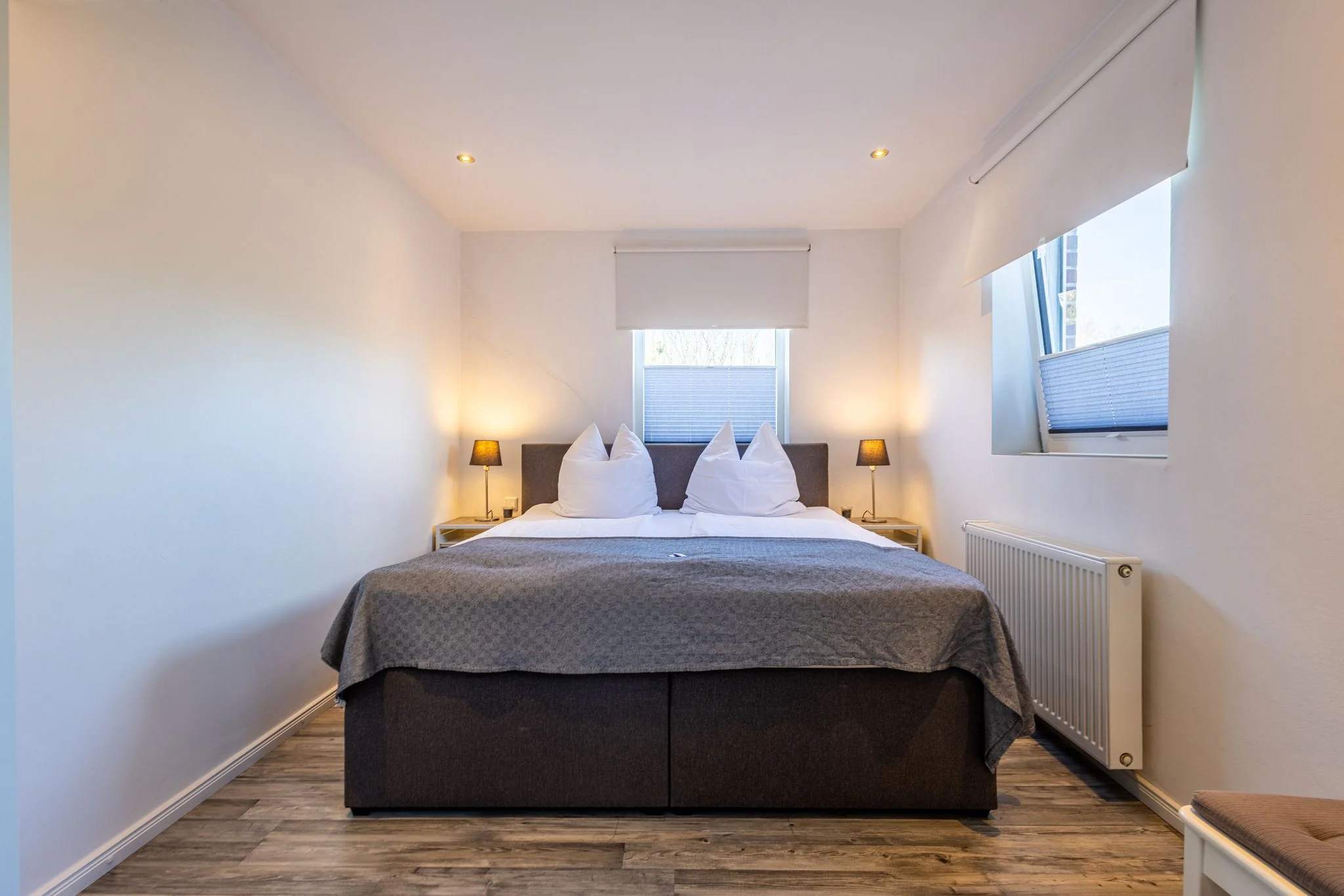 Modernes Schlafzimmer mit Doppelbett, grauer Tagesdecke, Holzboden und Rollos in Ferienwohnung