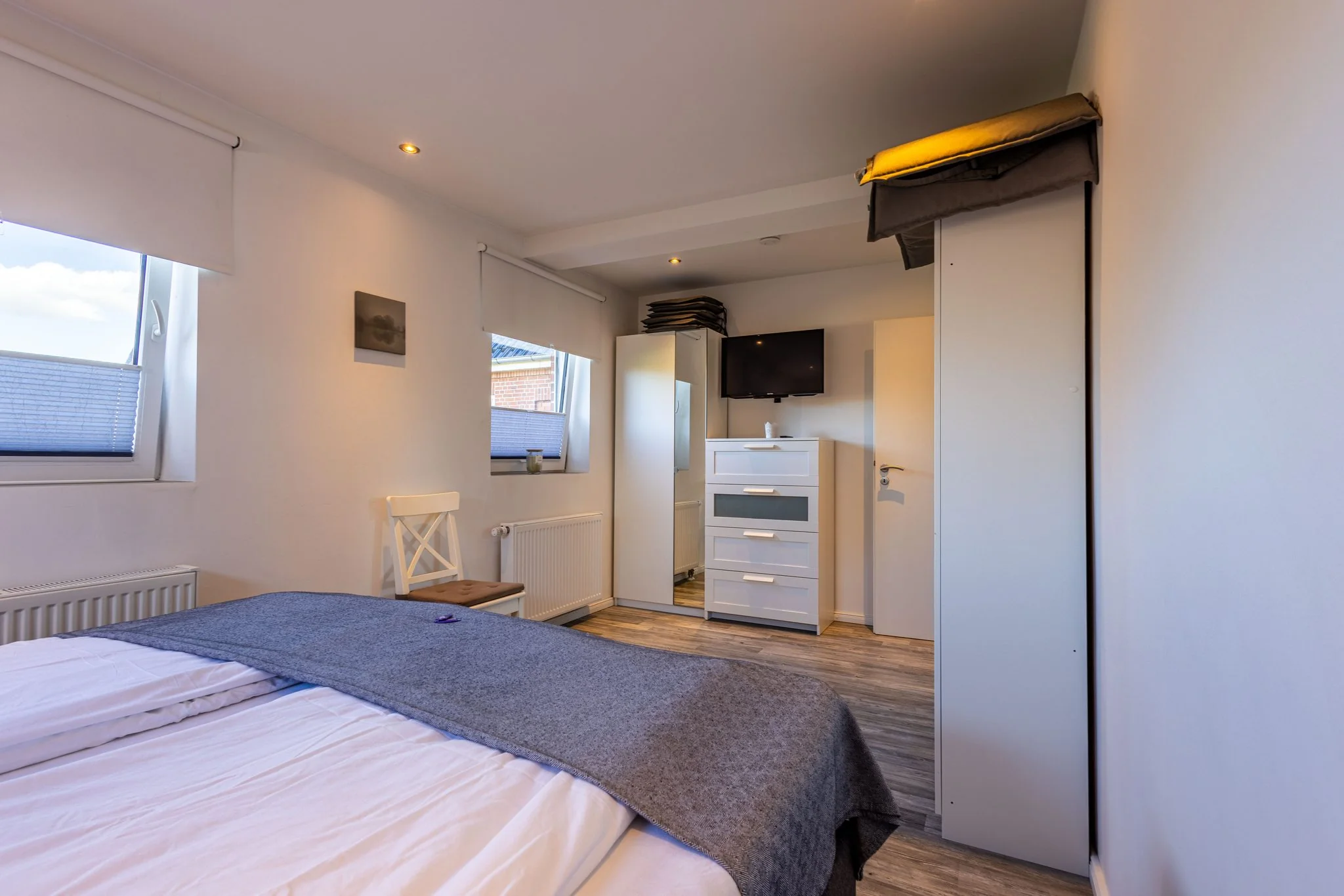 Helles Schlafzimmer mit Doppelbett, weißer Kommode, Kleiderschrank und TV in Ferienunterkunft