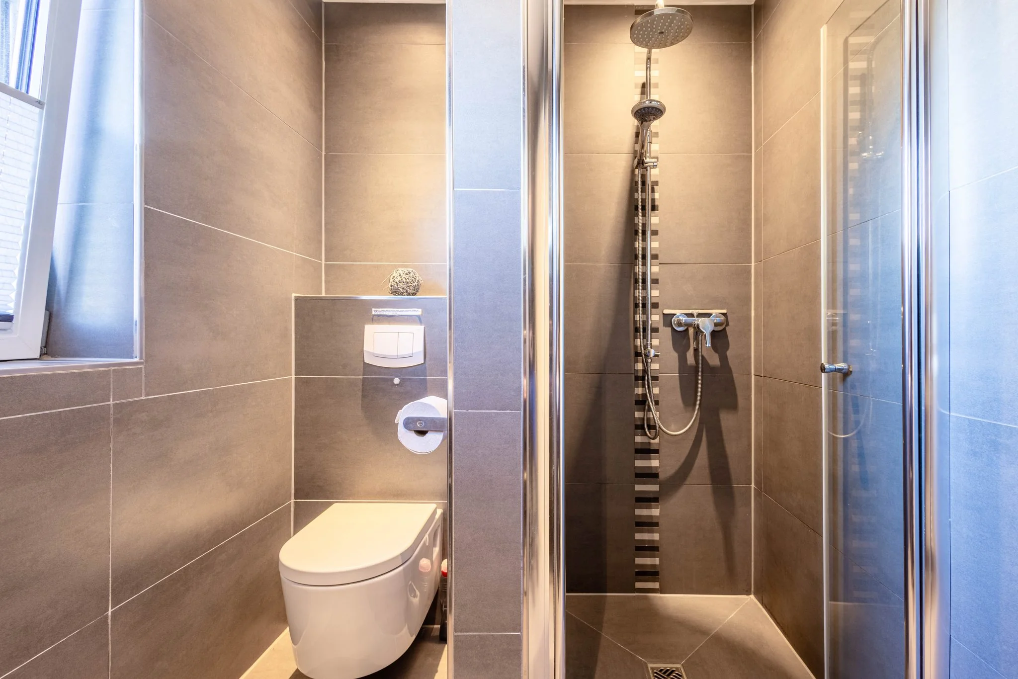 Modernes Badezimmer mit Duschkabine, Regendusche und Wand-WC in grauer Fliesenoptik